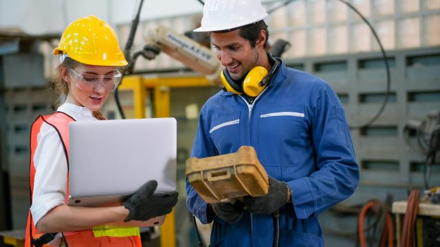 Factory worker man and woman with safety uniform discussion about robot working in factory workplace. They look happy with concept of good system and manager support for better industrial business.